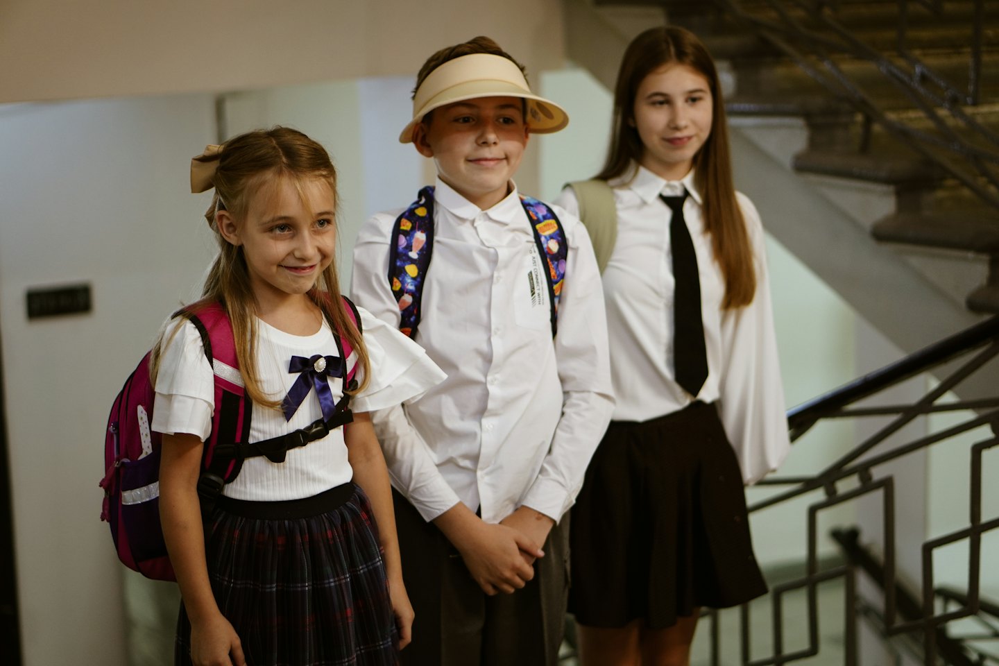 Tres niños sonrientes con uniformes escolares y mochilas.