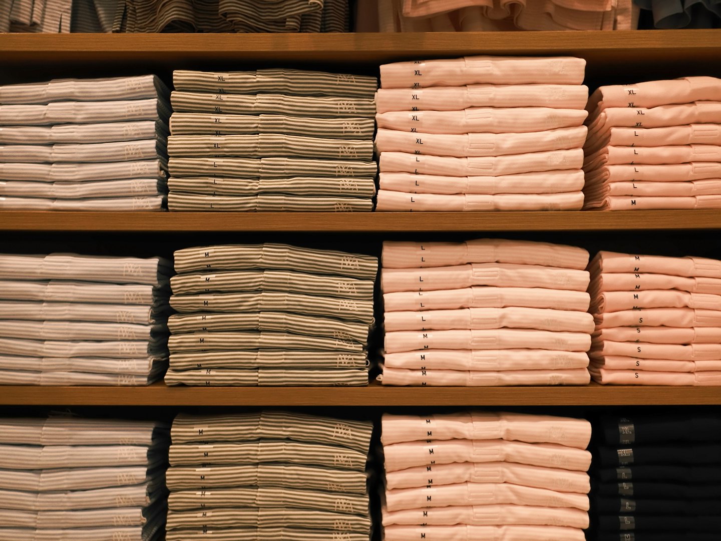 Camisetas dobladas y apiladas en estantes de madera de una tienda.