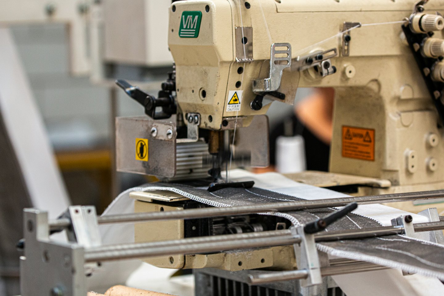 Una máquina de coser industrial cose tela negra sobre un textil blanco.