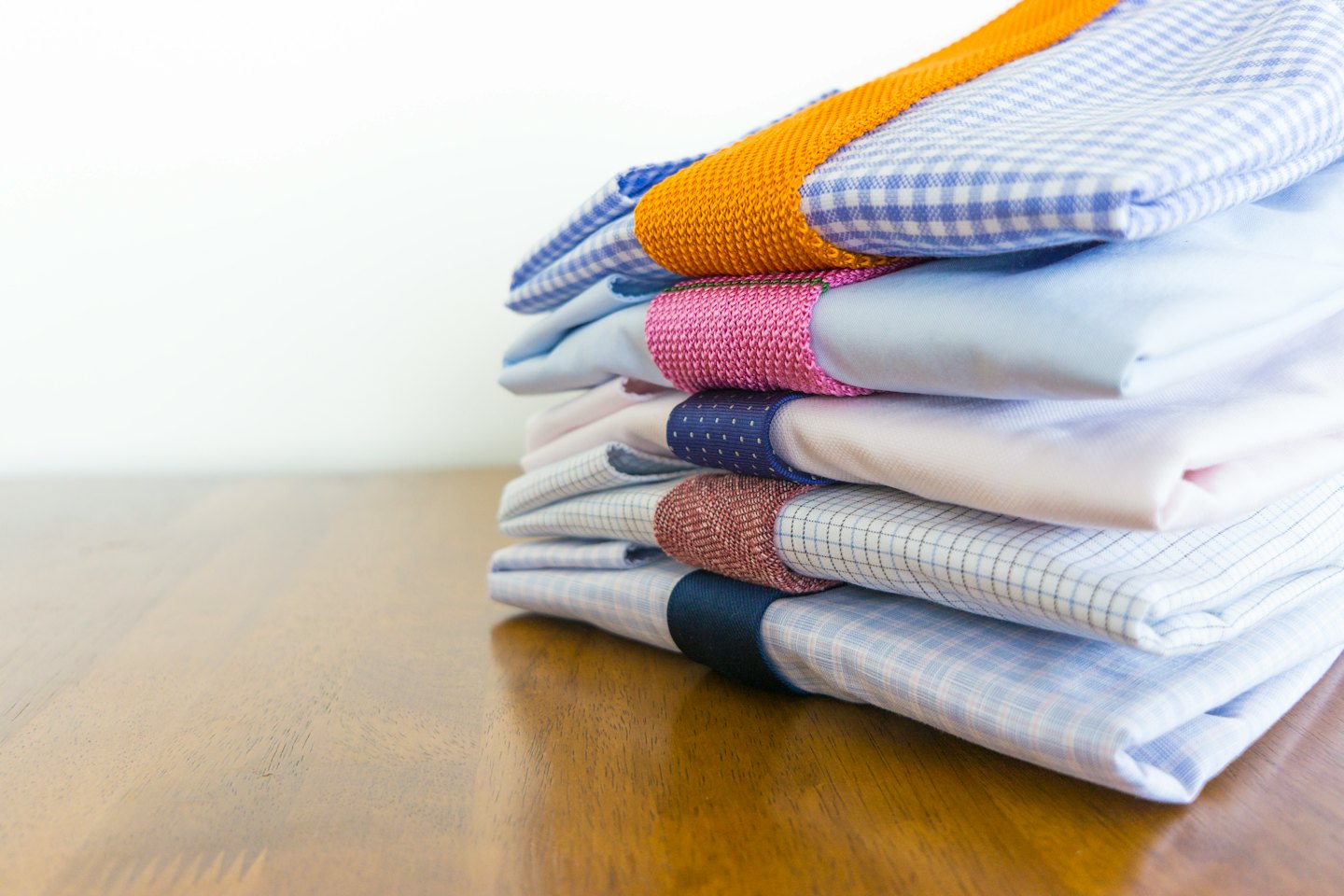 Cinco camisas de vestir dobladas y apiladas sobre una superficie de madera.