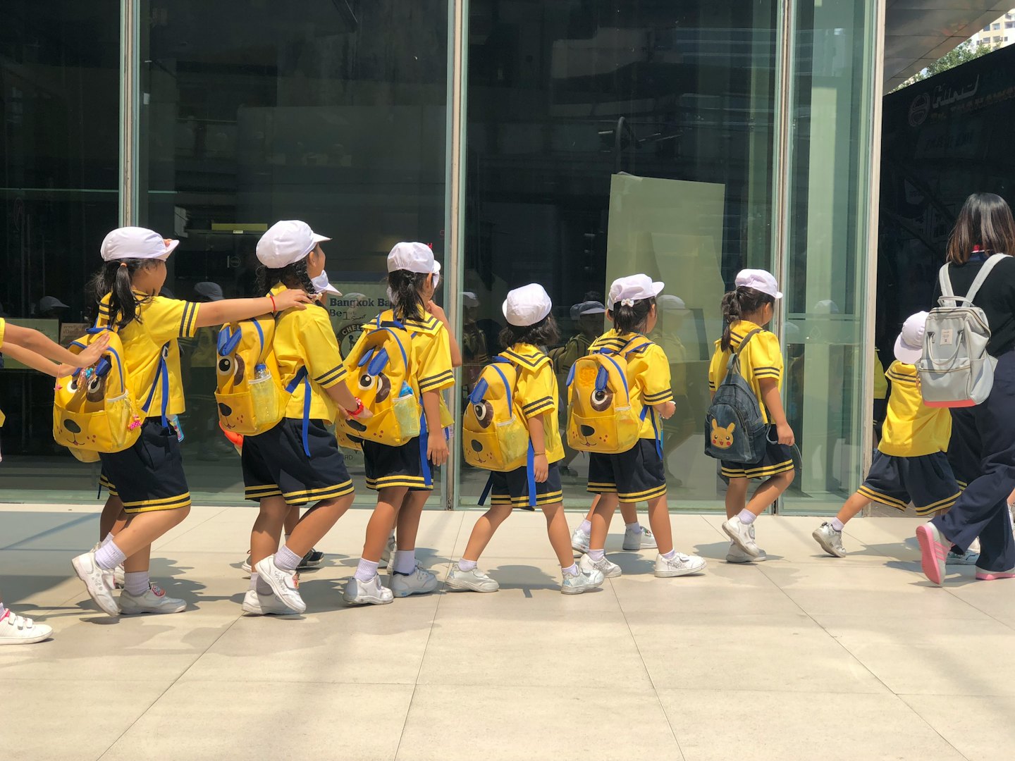Niños con uniforme escolar caminan con un adulto en un día soleado.
